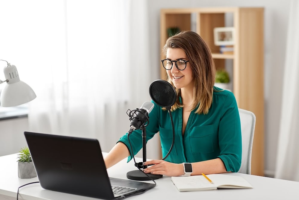 woman with a mic and spitscreen and laptop podcasting on a budget