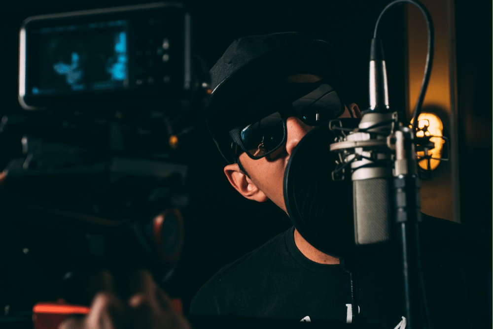 man with sunglasses talking into a microphone with a spit screen